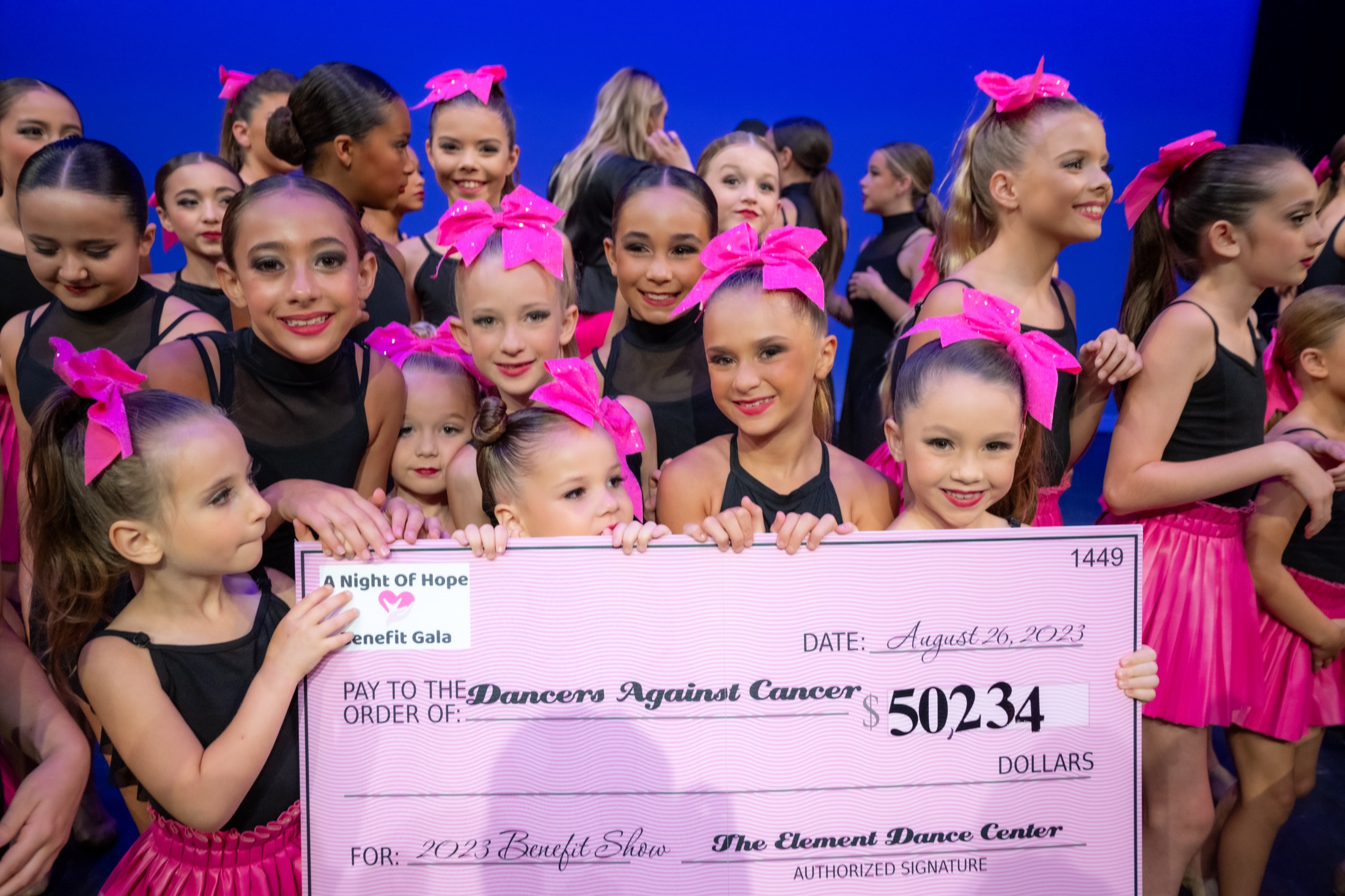 Young dancers on stage presenting a large donation check to Dancers Against Cancer