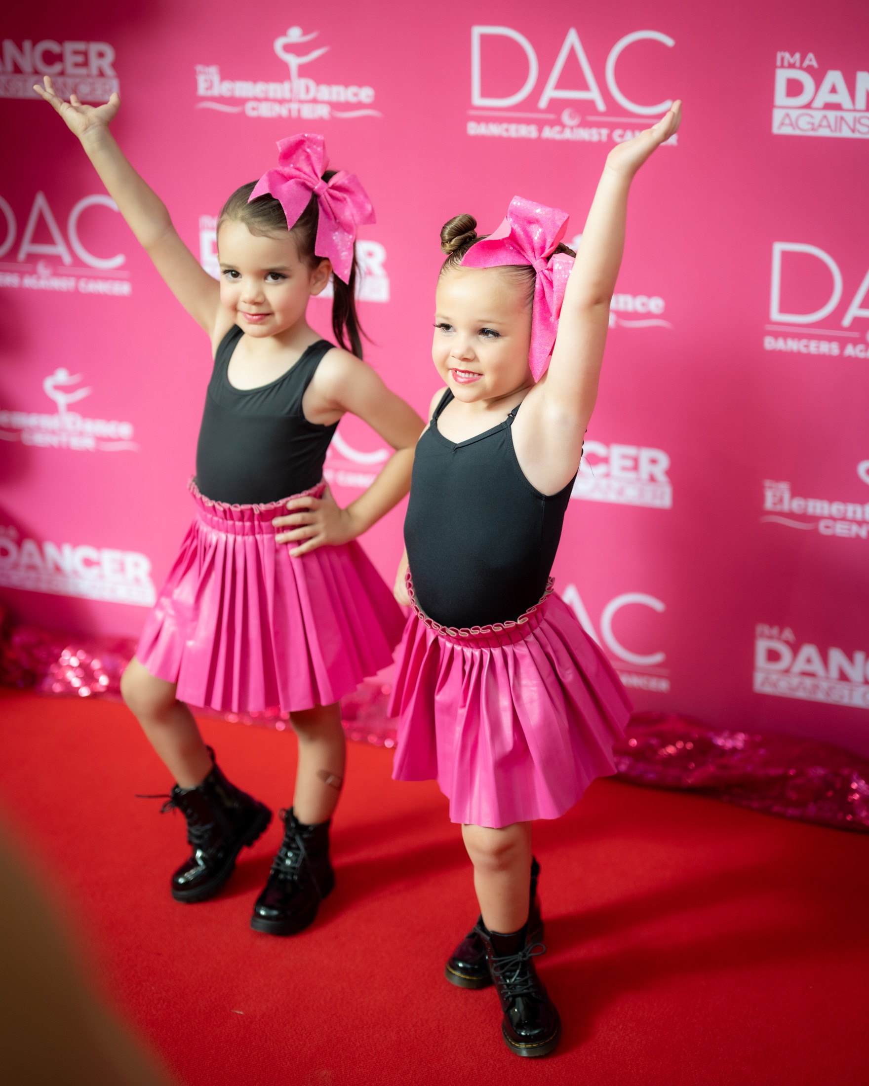 Two young dancers posing in front of a Dancers Against Cancer backdrop